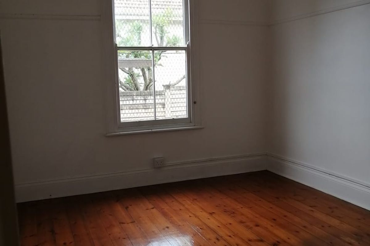 A bright, empty bedroom featuring polished timber flooring, classic picture rails, and a traditional sash window.