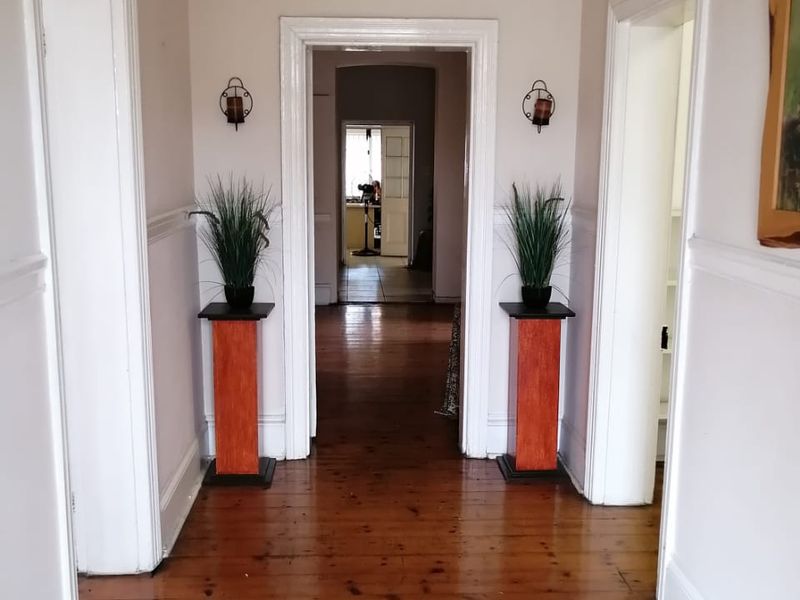 A spacious hallway featuring polished hardwood flooring, classic wainscoting, and wall sconces, providing a bright and welcoming transition between rooms.