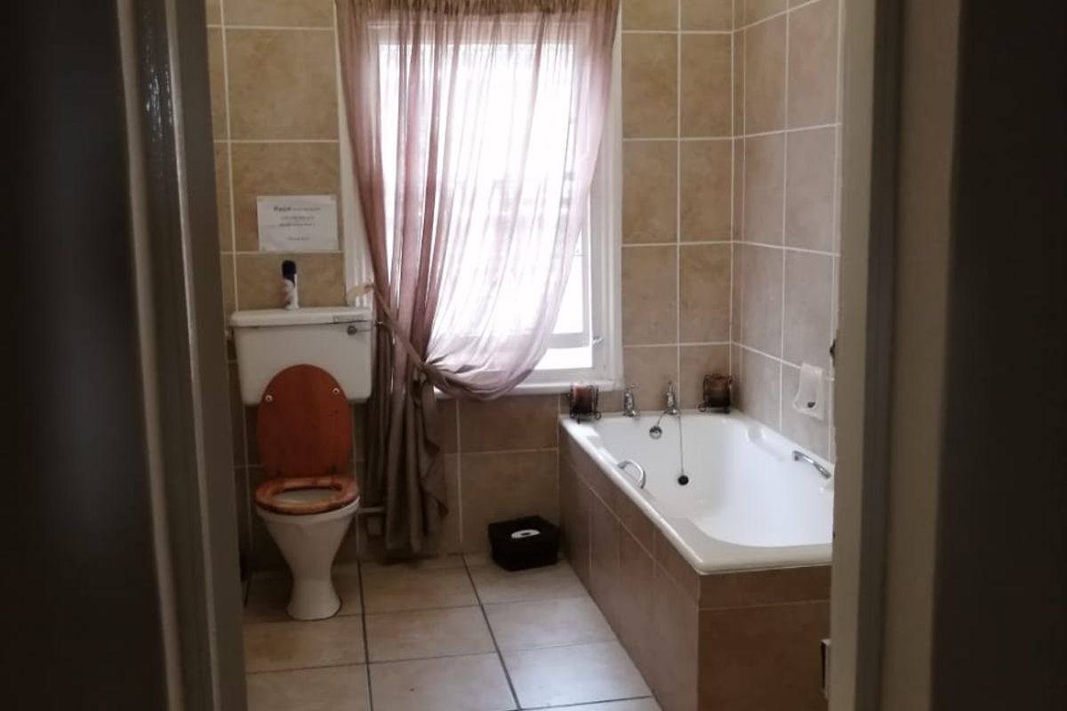 A functional bathroom featuring a built-in bathtub, ceramic wall and floor tiling, and a standard toilet, offering a neutral and practical layout.