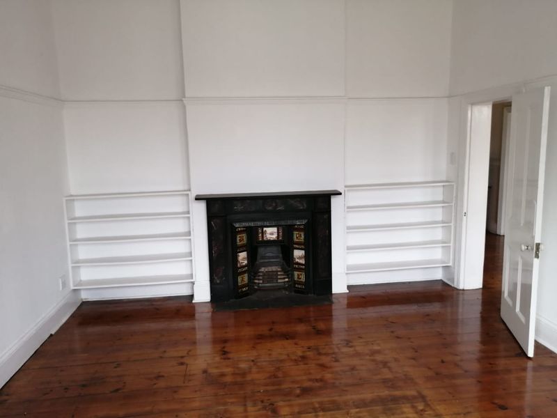 A bright, vacant living room featuring polished timber flooring, a classic ornate fireplace, and symmetrical built-in shelving units.