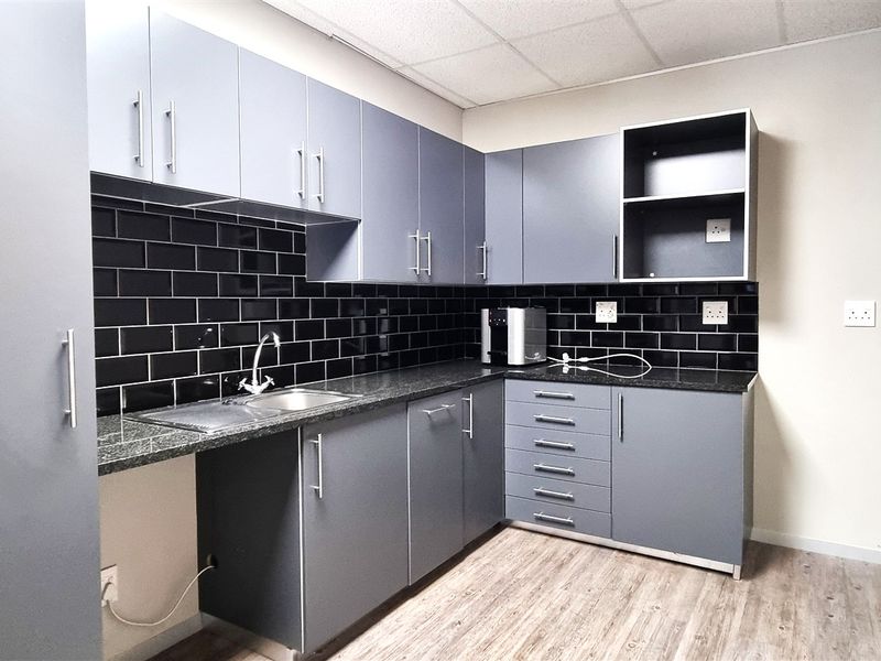 A functional office kitchenette featuring modern grey cabinetry, a dark granite countertop, and a stylish black subway tile backsplash.