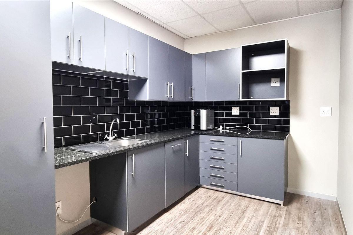 A functional office kitchenette featuring modern grey cabinetry, a dark granite countertop, and a stylish black subway tile backsplash.