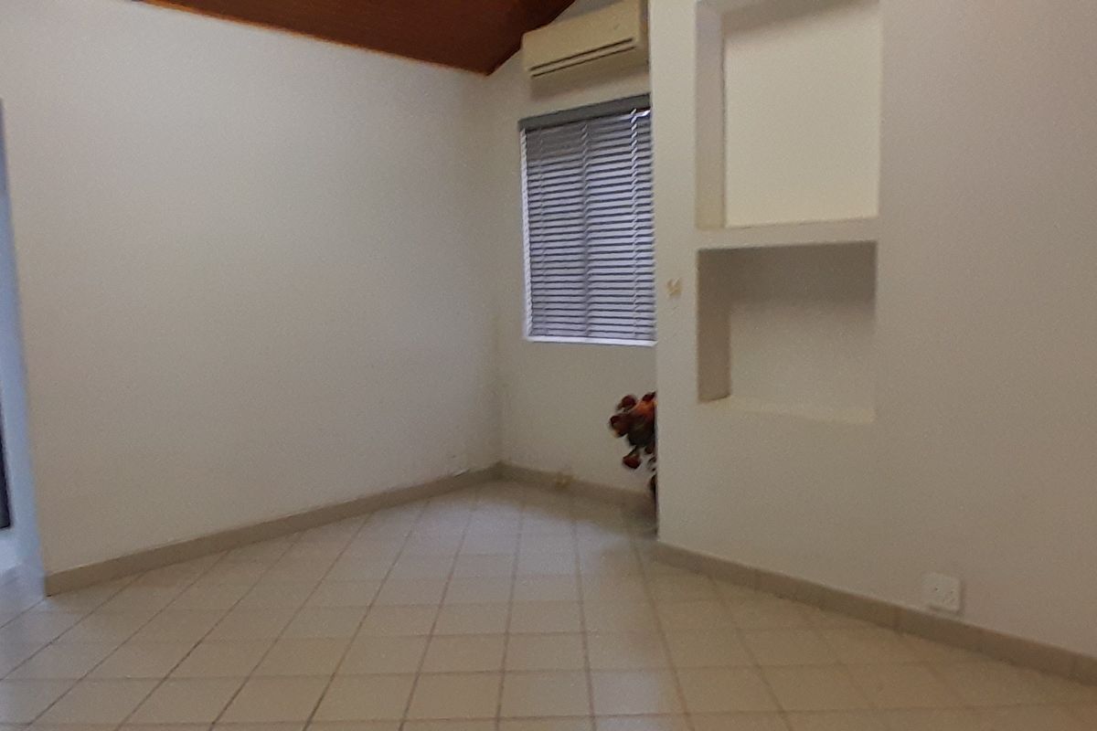An empty living area featuring tiled flooring, a vaulted ceiling, built-in wall niches, and a wall-mounted air conditioning unit.