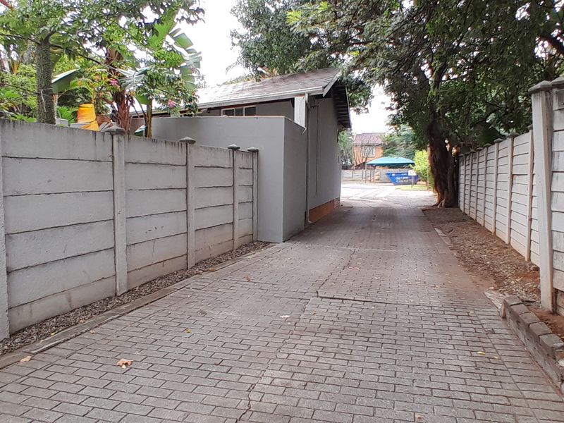 A paved driveway leading to the rear of the property, enclosed by precast concrete boundary walls and mature trees.