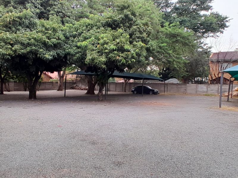 Spacious outdoor area featuring a gravel surface, mature trees, and multiple shade cloth carports enclosed by a precast concrete boundary wall.