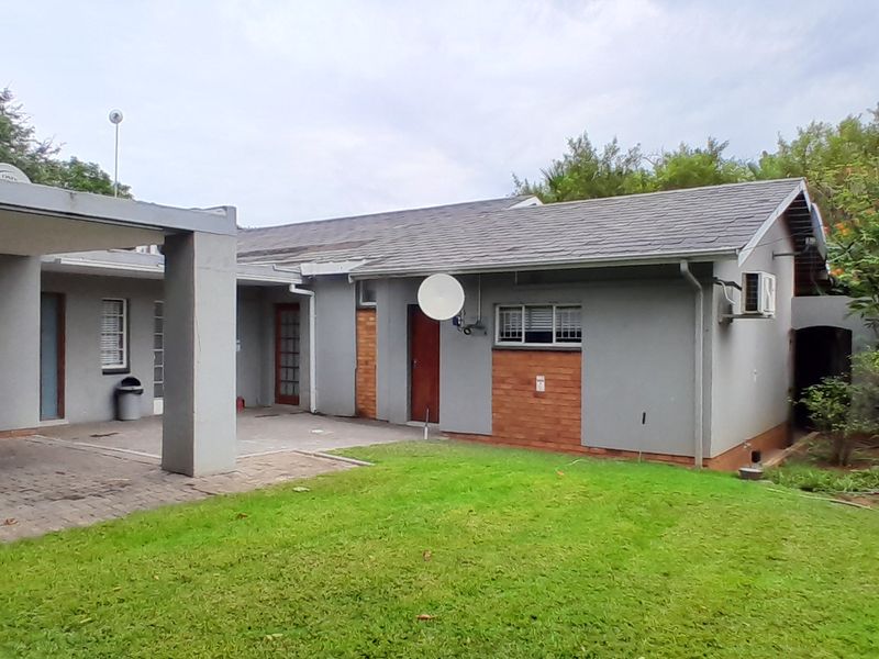Rear view of the property featuring a covered patio area, paved flooring, and a well-maintained garden with brick boundary walling.