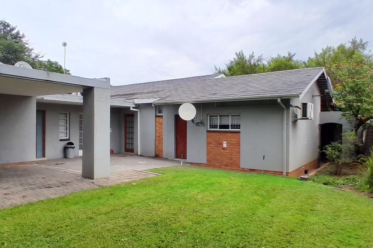 Rear view of the property featuring a covered patio area, paved flooring, and a well-maintained garden with brick boundary walling.