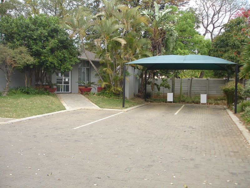 Front exterior view of the property featuring a paved parking area, a shade cloth carport, and established garden landscaping.