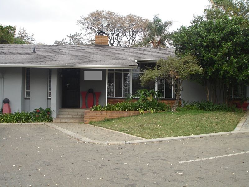 Front exterior view of a single-story commercial building featuring a paved driveway, brick retaining wall, and a tiled roof with a chimney.