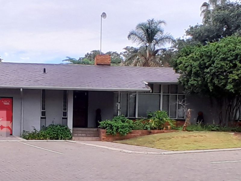 Front exterior view of a single-story commercial property featuring a paved driveway, brick landscaping elements, and a pitched roofline.