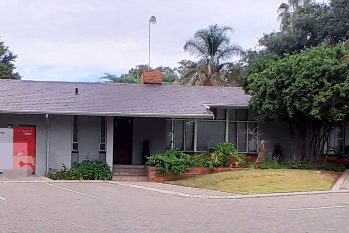 Front exterior view of a single-story commercial property featuring a paved driveway, brick landscaping elements, and a pitched roofline.
