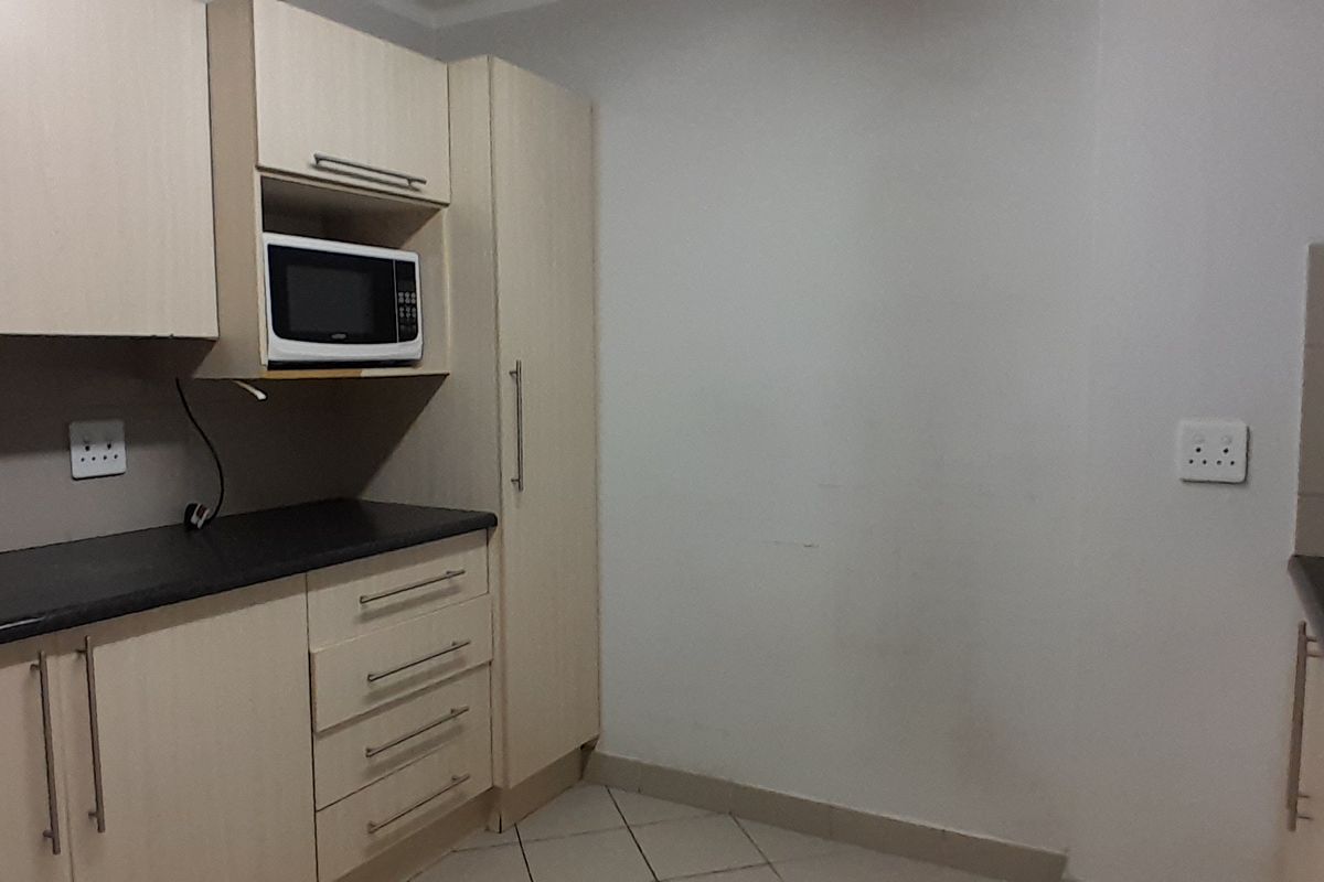 A functional kitchen area featuring light-toned built-in cabinetry, dark laminate countertops, and tiled flooring, providing a clean and practical workspace.