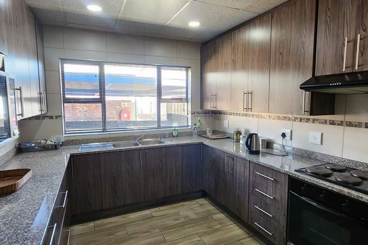 A well-maintained kitchen featuring dark wood cabinetry, granite countertops, a built-in oven, hob, and extractor fan with tiled flooring.