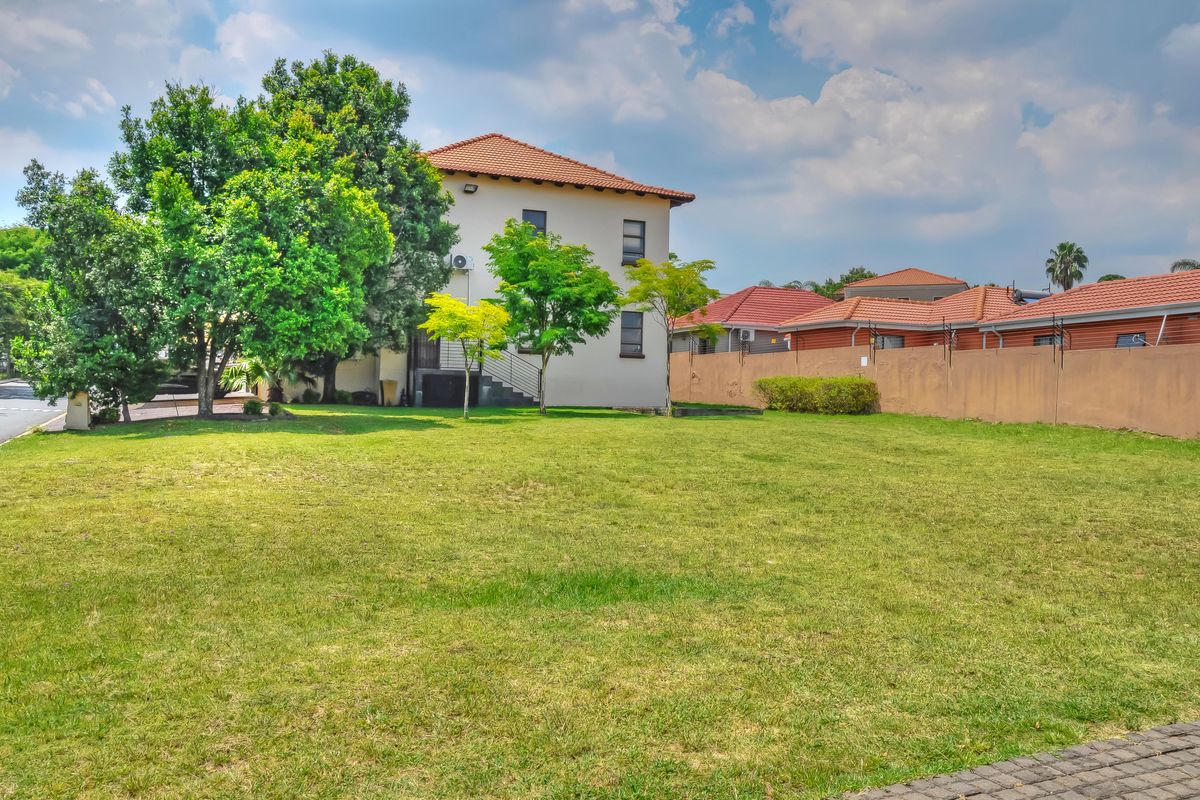 A spacious rear garden area featuring a well-maintained lawn, mature trees, and a perimeter boundary wall, providing a private outdoor space.