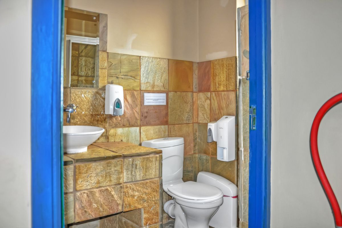 A compact office restroom featuring natural stone wall tiling, a built-in stone vanity with a vessel sink, and a standard toilet.