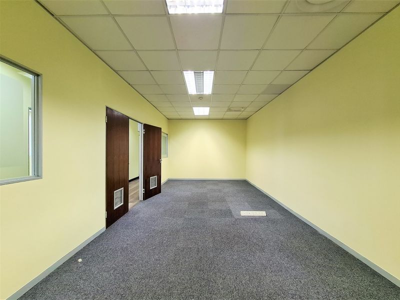 A vacant office space featuring carpeted flooring, a suspended ceiling with recessed lighting, and double door access.