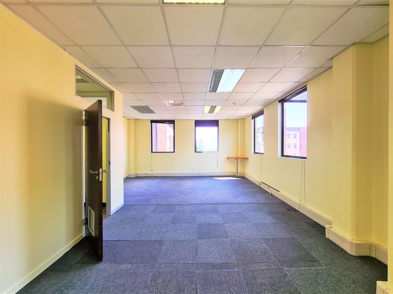 A vacant, open-plan office space featuring suspended ceilings, recessed lighting, and carpeted flooring with natural light from multiple windows.