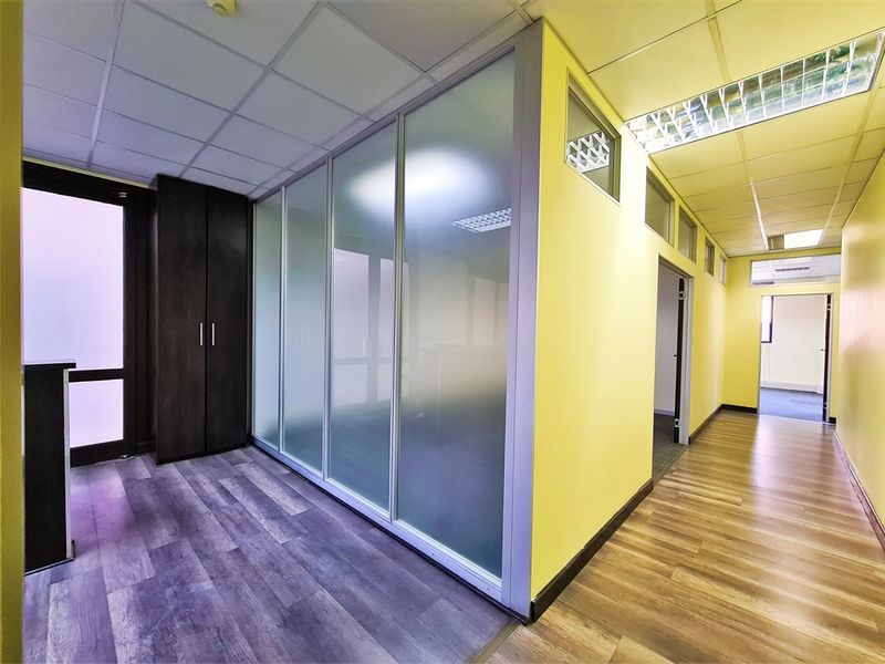 Modern office space featuring a frosted glass partition, suspended ceiling with recessed lighting, and durable laminate flooring with built-in storage.
