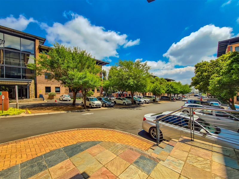 Exterior view of the office complex featuring a paved parking area, landscaped trees, and a modern brick and glass building facade.