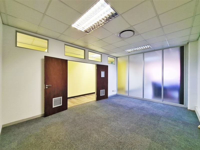 A bright, empty office space featuring a suspended ceiling, carpeted flooring, and a frosted glass partition wall, offering a clean and professional work environment.