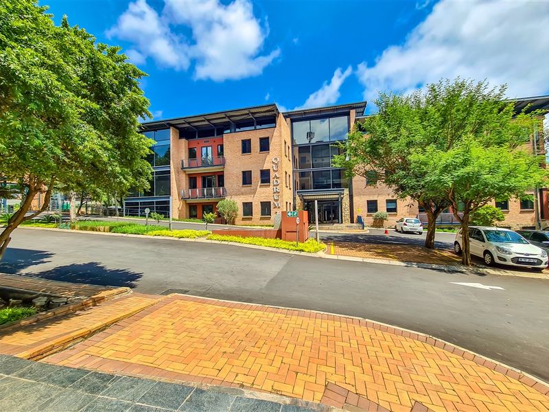 Front exterior view of the Quadrum office building featuring a modern brick and glass facade with integrated balconies and surrounding landscaped grounds.