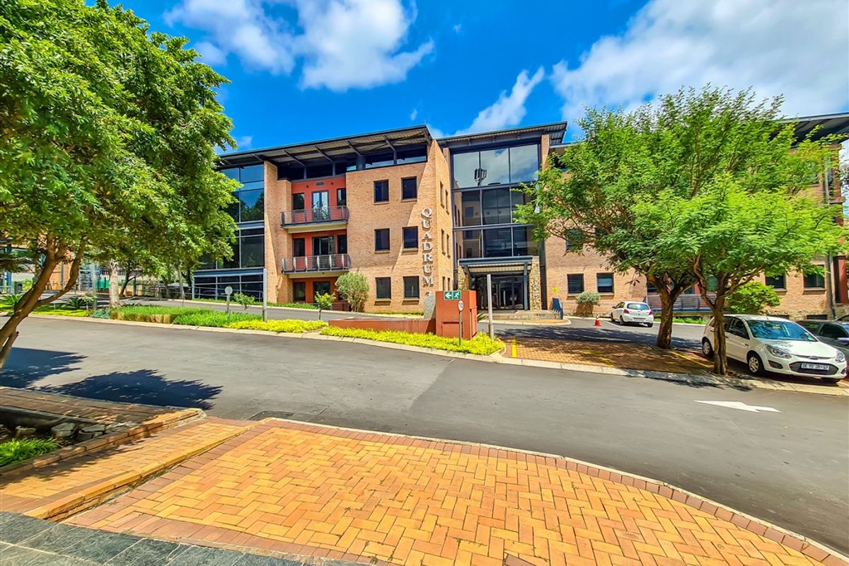 Front exterior view of the Quadrum office building featuring a modern brick and glass facade with integrated balconies and surrounding landscaped grounds.