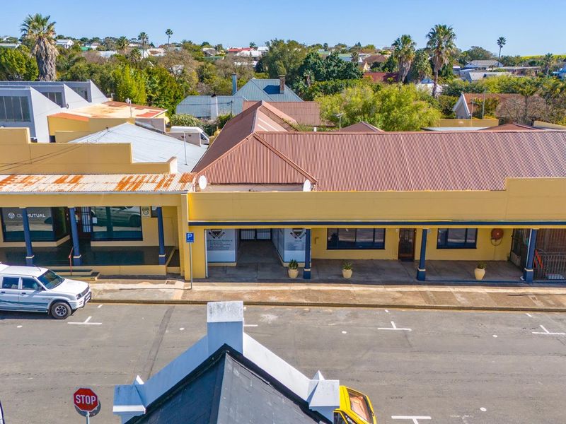 Aerial view of a commercial property featuring a corrugated metal roof, covered walkway with support columns, and street-level access in a suburban setting.