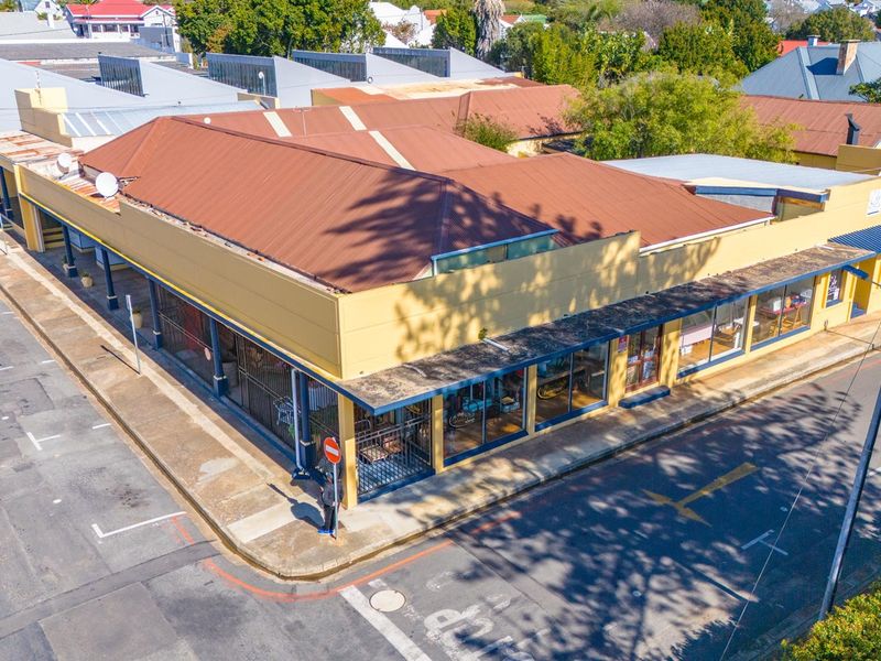 Aerial view of a corner commercial property featuring a corrugated metal roof, covered walkways, and large street-facing display windows.