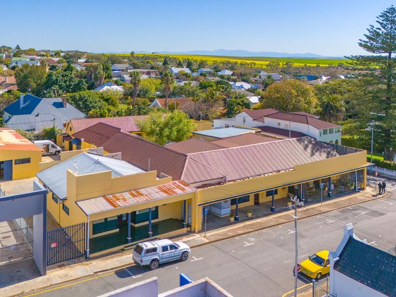 Aerial view of a commercial property featuring a metal roof, covered veranda, and street-level access within a suburban neighborhood setting.