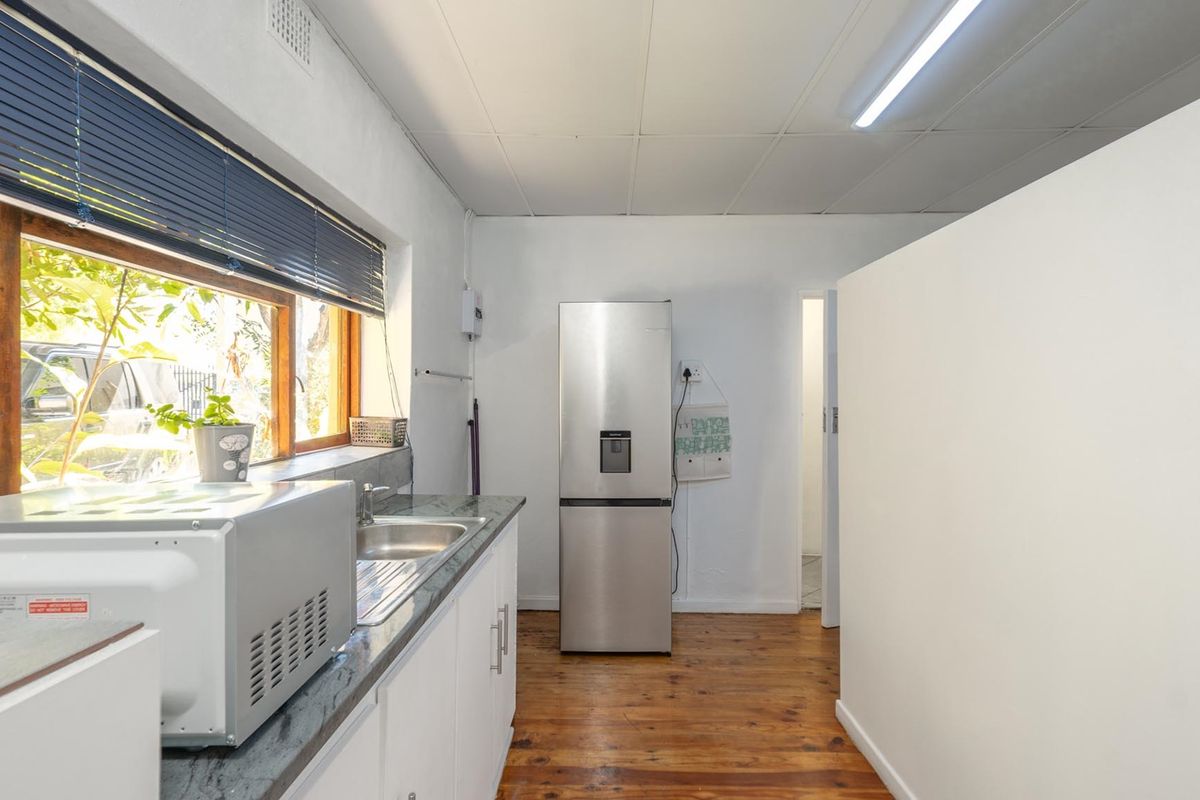 A functional kitchen area featuring timber flooring, built-in cabinetry with laminate countertops, a stainless steel sink, and a drop ceiling with fluorescent lighting.