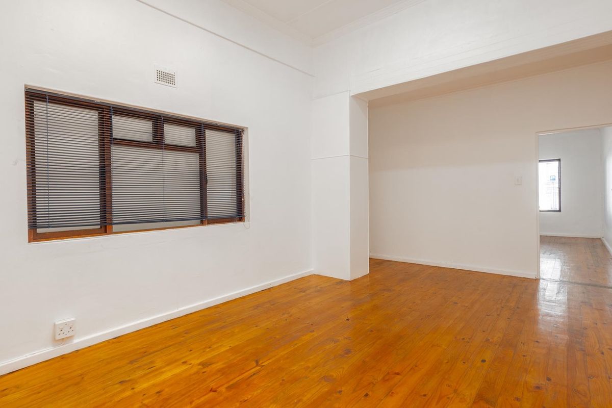 An empty, well-lit living area featuring polished timber flooring, white walls, and venetian blinds, offering a clean and versatile space for commercial use.