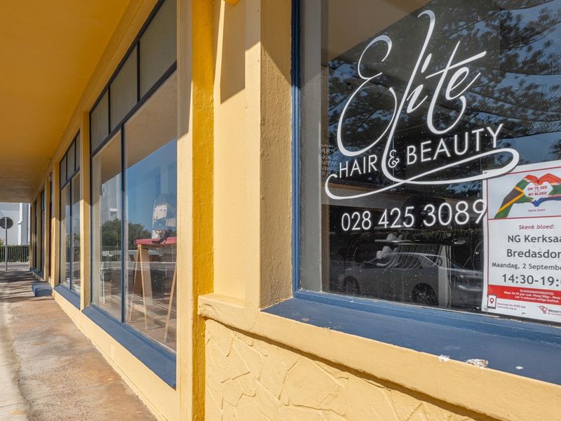 Commercial storefront featuring large display windows and a covered walkway, currently occupied by a hair and beauty salon.