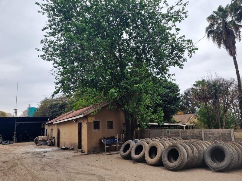 Exterior view of a farm outbuilding featuring a tiled roof and concrete boundary wall, situated on a dirt yard area.