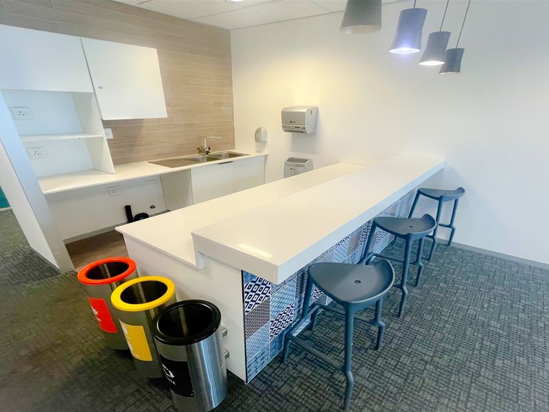 A modern office kitchenette featuring a stone breakfast bar, decorative tiled base, stainless steel sink, and contemporary pendant lighting.