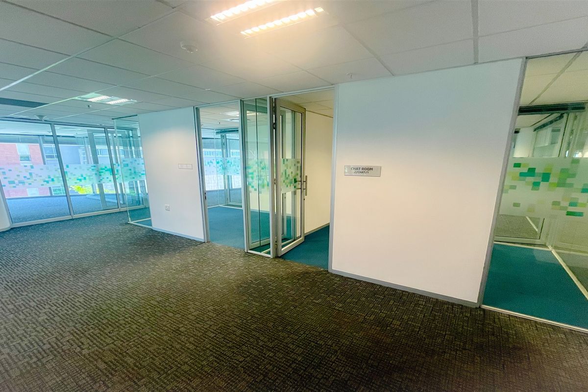 Modern office space featuring glass partition walls, carpeted flooring, and recessed lighting, providing a clean and professional environment for business operations.
