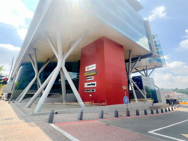 Modern commercial office building featuring a striking architectural design with glass facade, prominent red structural core, and integrated corporate signage.