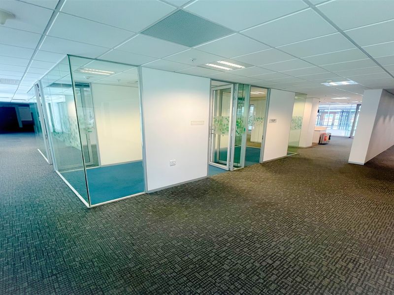 Spacious open-plan office area featuring modern glass-partitioned meeting rooms, suspended ceilings, and durable carpeted flooring throughout.