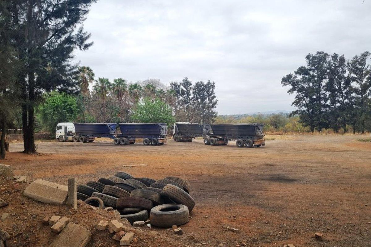 Expansive unpaved yard area on the farm property, featuring mature trees and open space suitable for heavy vehicle access or storage.