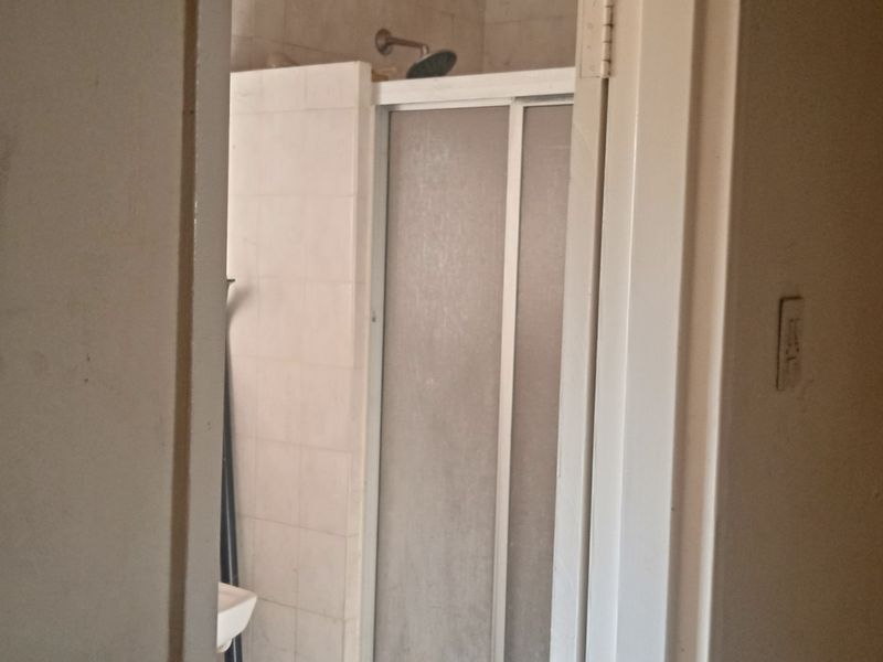 A view into a dated bathroom featuring a shower enclosure with tiled walls, requiring cosmetic updates to improve its overall condition.