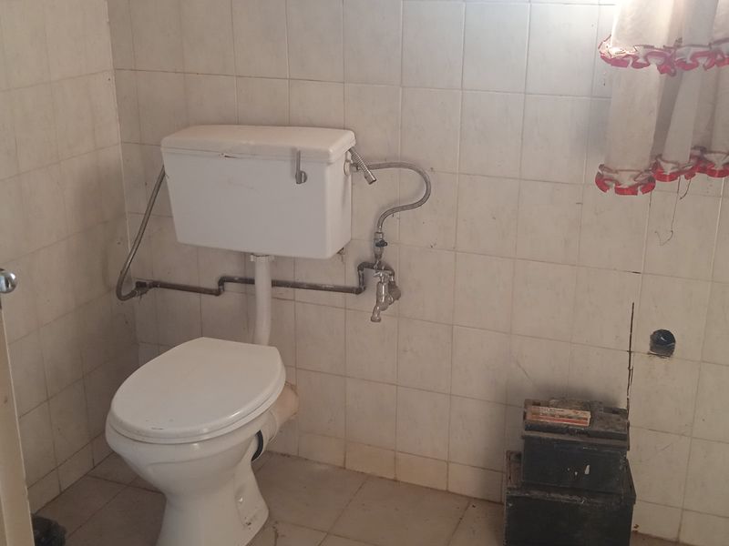A dated bathroom featuring a pedestal basin and toilet with exposed plumbing and damaged wall tiling, requiring renovation to modernize the space.