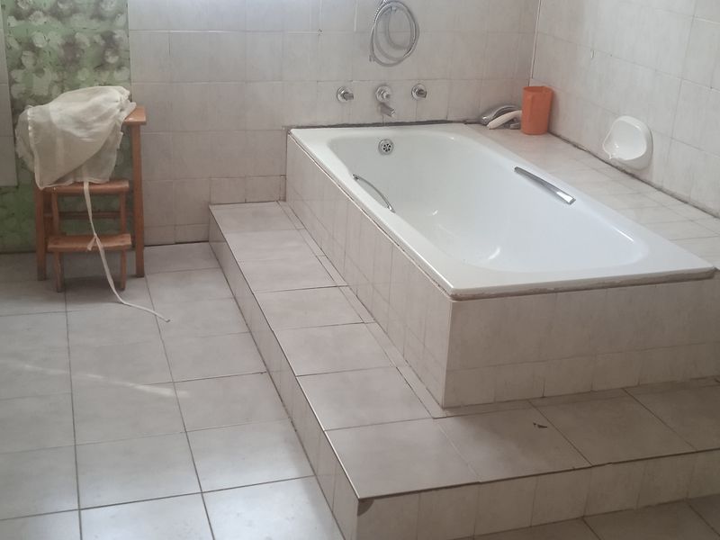 A dated bathroom featuring a pedestal basin and a built-in tiled bathtub with full wall tiling, requiring cosmetic updates to modernize the space.