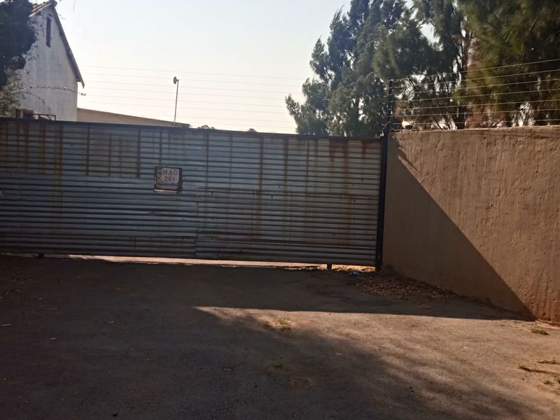 A gated entrance to the property featuring a metal sliding gate, perimeter walling with electric fencing, and an asphalt driveway.