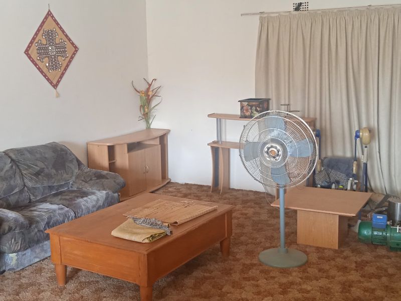 A living room area featuring carpeted flooring and a curtained window, offering a blank canvas for potential interior updates and modernization.
