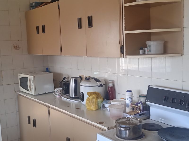 A dated kitchen featuring original built-in cabinetry, tiled backsplash, and a freestanding electric stove, offering potential for a modern renovation.