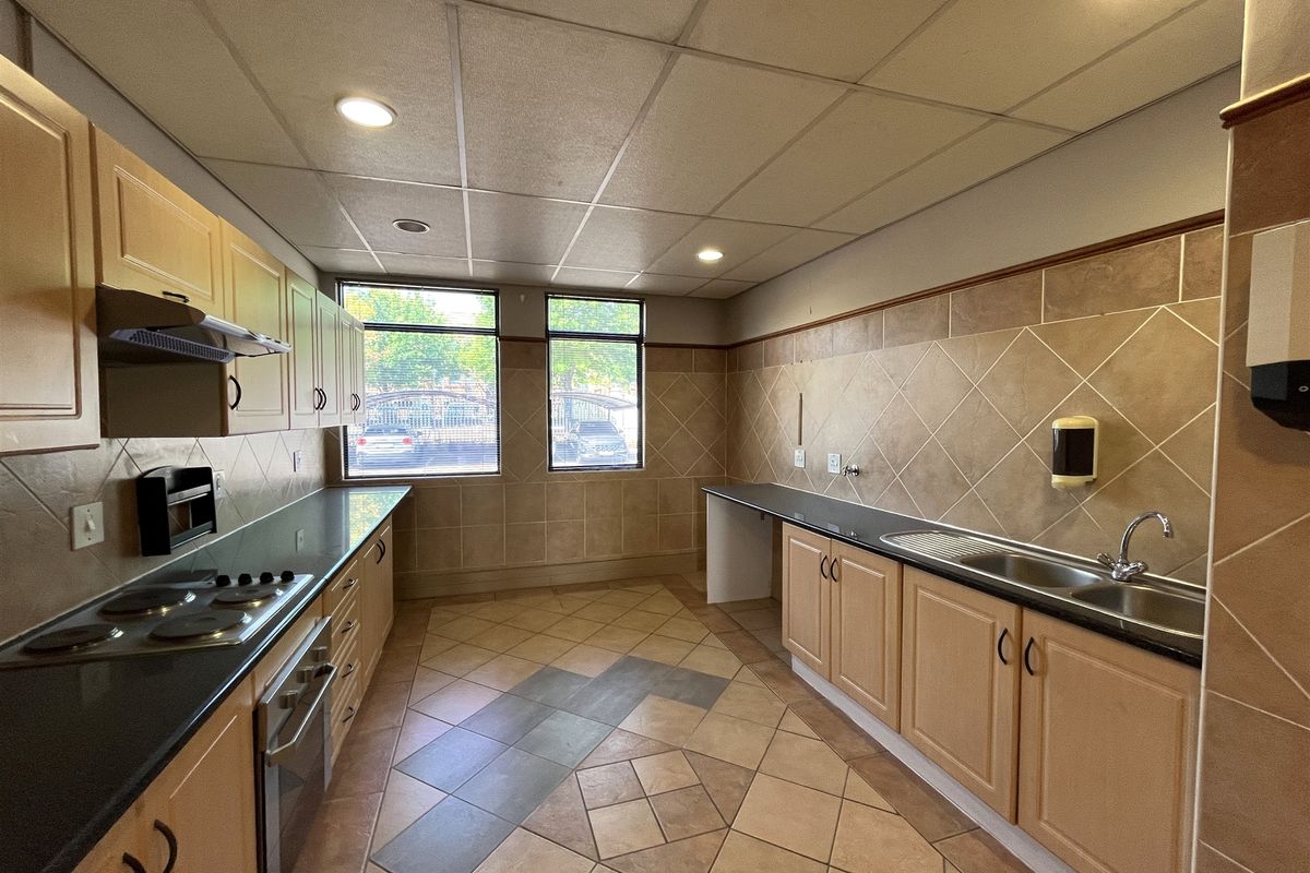 A functional office kitchenette featuring built-in cabinetry, a stainless steel sink, integrated electric hob and oven, and tiled wall finishes.