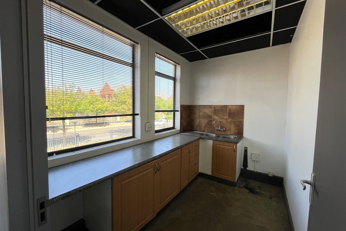 A functional office kitchenette featuring built-in wooden cabinetry, granite-look countertops, a stainless steel sink, and a tiled backsplash.