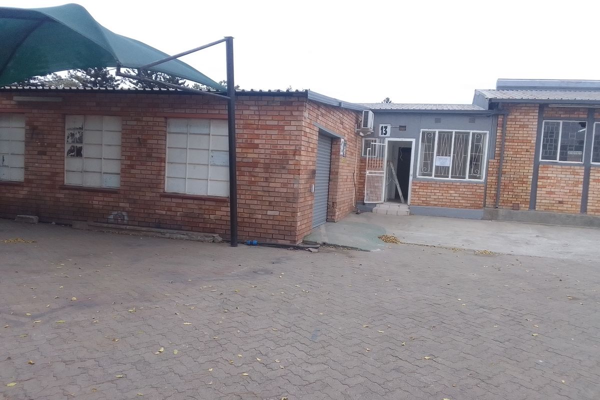 Front exterior view of an industrial property featuring brick facade, paved driveway, security gates, and a roller shutter door.