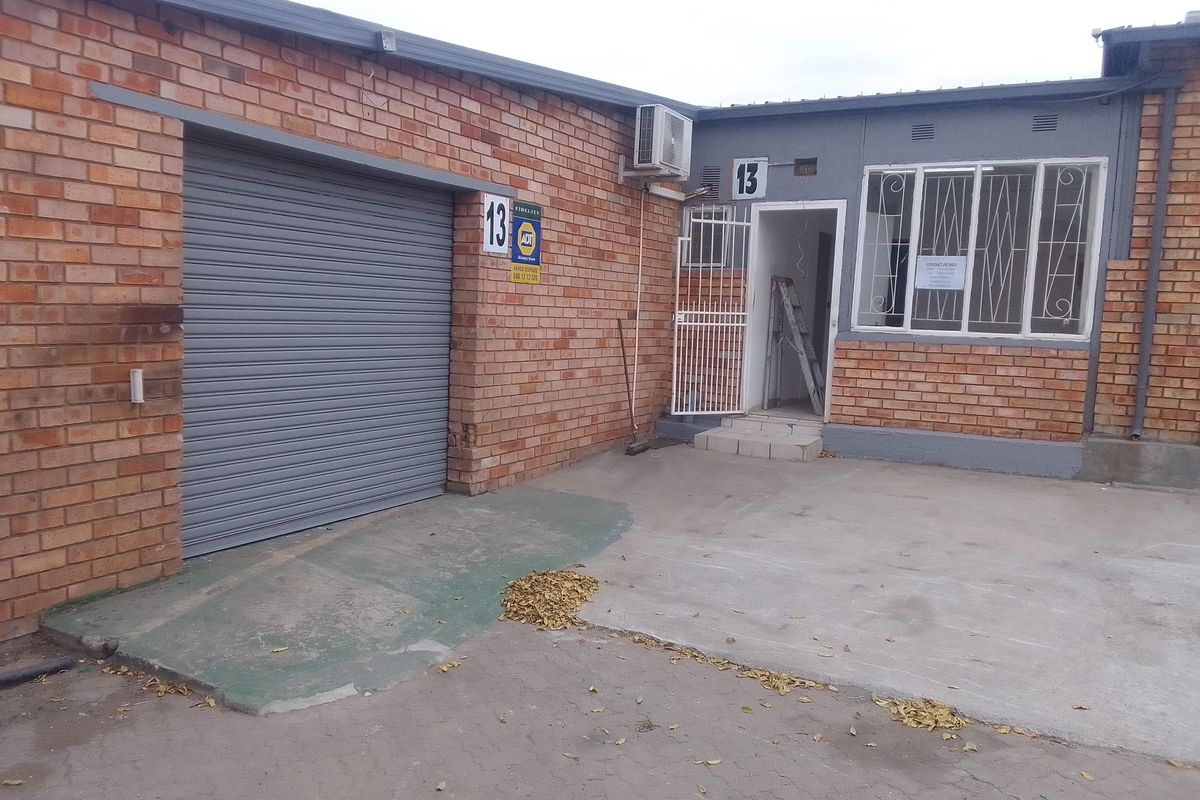 Industrial unit exterior featuring a roller shutter door, security gate, and brick facade with an integrated air conditioning unit.