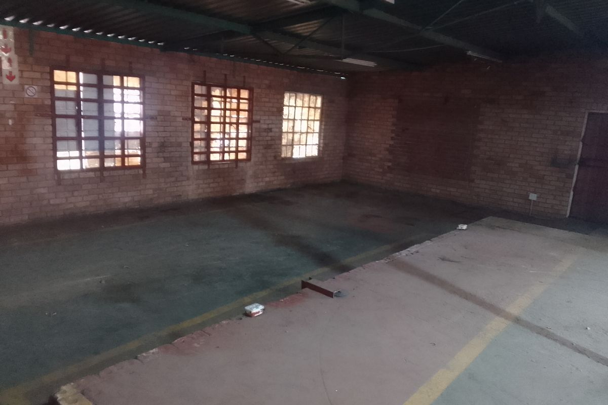 An empty industrial utility space featuring exposed brick walls, metal roof trusses, and concrete flooring with industrial-style windows.