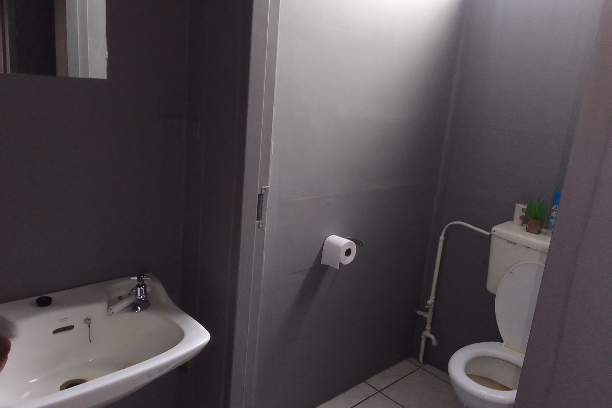 A functional bathroom featuring a pedestal basin, chrome faucet, and standard toilet with ceramic floor tiling and grey painted walls.